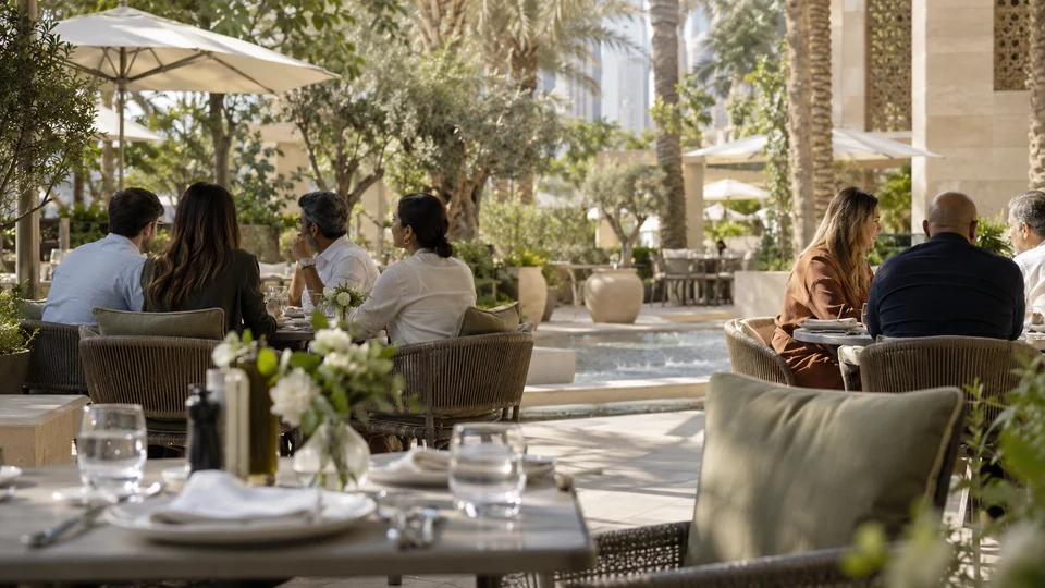 Illustrative team lunch on a leafy Dubai terrace, with colleagues gathered around outdoor tables.